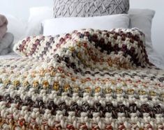 a crocheted blanket sitting on top of a bed next to pillows and blankets