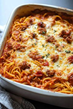 a casserole dish with spaghetti and meat in it on a towel next to a fork