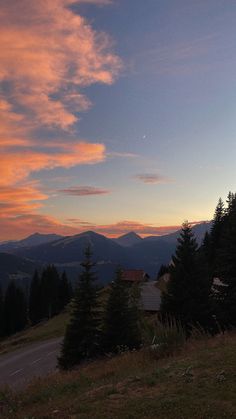 the sun is setting in the mountains with trees on the side and a road running through it