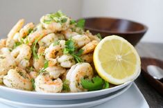 a white bowl filled with shrimp and garnished with herbs next to a slice of lemon