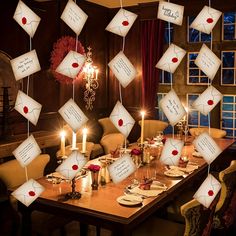 a dining room table with many envelopes hanging from the ceiling and candles in front of it