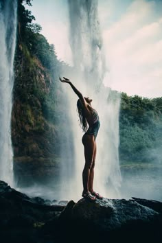 a woman standing in front of a waterfall with her arms up and legs spread out