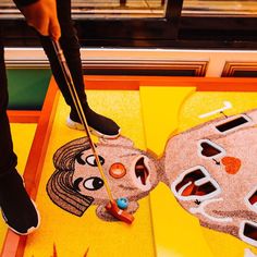 a person standing on top of a colorful floor next to a table with an odd face painted on it