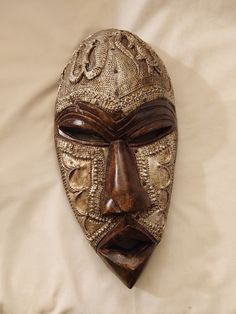 a wooden mask with intricate designs on it's face and eyes, resting on a white sheet