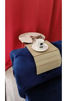 a table with a cup and saucer sitting on top of it next to a red curtain