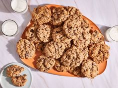 an orange plate with cookies and two glasses of milk next to it on a white table