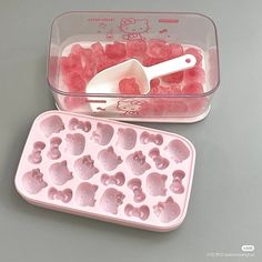 a plastic container filled with ice cubes next to a plastic tray full of pink gummy bears