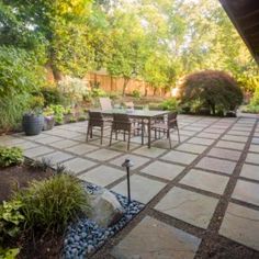 an outdoor patio with table and chairs surrounded by trees, shrubs and rocks in the foreground