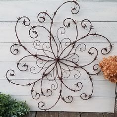 a metal wall hanging on the side of a white building with a plant next to it