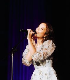 a woman in a white dress singing into a microphone