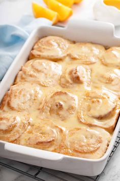 a white casserole dish filled with cinnamon rolls and orange slices on a cooling rack