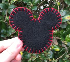 someone is holding up a mickey mouse felt piece in front of some bushes and trees