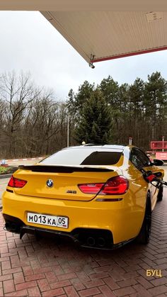 a yellow car parked in front of a gas station with its trunk open and the hood up