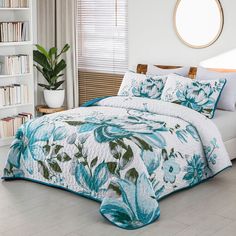 a bed with blue flowers on it in a room next to bookshelves and a round mirror