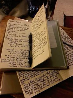 three notebooks with writing on them sitting on top of a wooden table next to a pen