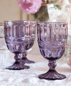 three glass goblets sitting on a table with pink flowers in the back ground