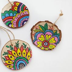 three wooden ornaments with colorful designs are hanging from strings on a white surface and one is decorated with wood slices