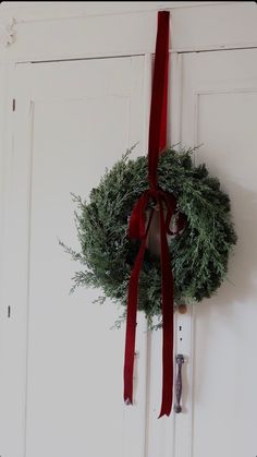 a christmas wreath hanging on the door with a red ribbon and bells attached to it