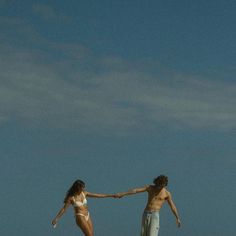 two people on the beach holding hands and flying a kite in the sky above them