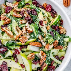 a salad with apples, cranberries and pecans in a large white bowl