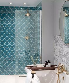 a white bath tub sitting under a bathroom mirror next to a sink and shower faucet