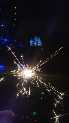 a person holding a sparkler in their hand with lights on the other side of it