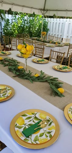 the table is set with yellow plates and lemons on them, along with greenery