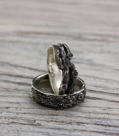 two silver rings sitting on top of a wooden table next to each other and one has a tree branch in the middle