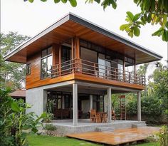 a modern house with wooden decking and balconys on the top floor, surrounded by greenery