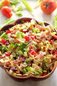 a bowl filled with pasta salad next to lettuce and tomatoes