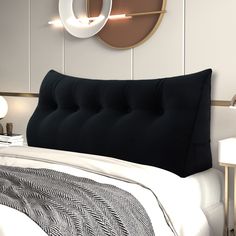 a bed with a black headboard and pillows on it next to two wall lights