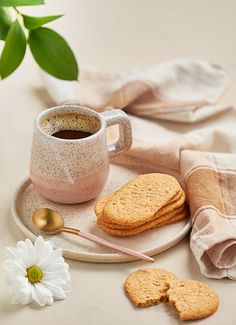 a cup of coffee and some cookies on a plate with a flower next to it