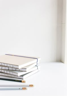 three books stacked on top of each other with pencils next to them