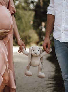 a pregnant woman holding the hand of a man who is holding a stuffed animal in front of her