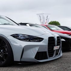 the front end of a white car parked in a lot with other cars behind it