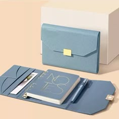 a blue folder with a notepad and pen in it next to a white box