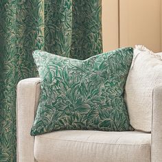 a green and white pillow sitting on top of a couch next to a window covered in curtains