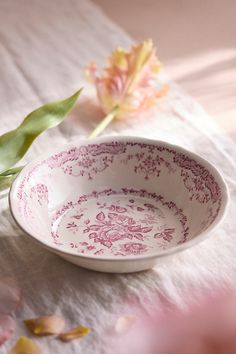 a pink and white bowl sitting on top of a table next to a flower vase