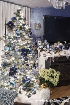 a living room decorated for christmas with blue and white ornaments on the tree, fireplace mantel and television