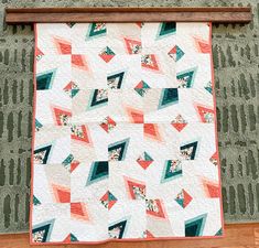 a quilt hanging on the wall next to a wooden frame with an orange and green geometric design