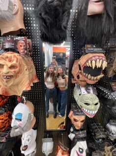 a woman taking a selfie in the mirror with several masks on display behind her