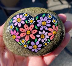 a painted rock in the shape of a heart with flowers on it is held by someone's hand