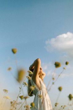 a woman standing in a field with her arms up to the sky and looking up