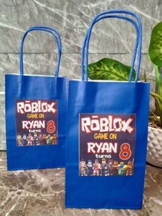 two blue bags with roblox game on them are sitting on a table next to a potted plant