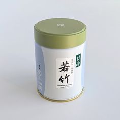 a canister with chinese writing on it sitting on a white surface, next to a green lid