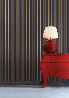 a red dresser with a lamp on top and striped wallpaper in the back ground