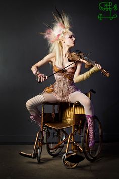 a woman in costume playing the violin on a wheel chair