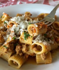 a white plate topped with pasta covered in meat and cheese next to a fork on top of it