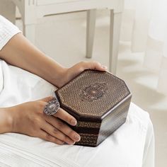 a woman's hand holding an ornate wooden box on top of a white bed