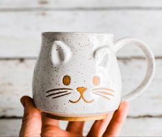 a hand holding a coffee mug with a cat face on it